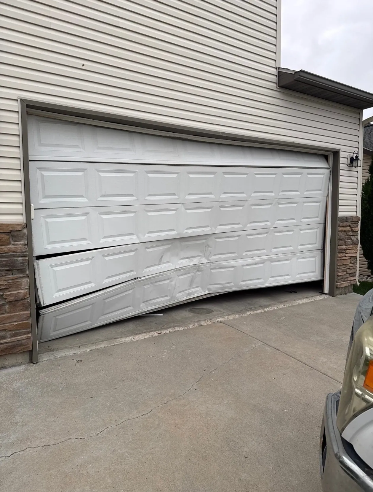 Damaged garage door hanging off track after coming loose